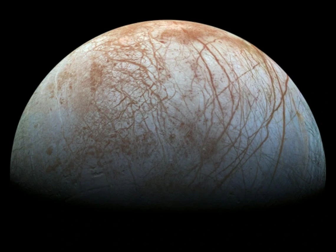 Jupiter's moon Europa is seen in this photograph. Its grey, icy surface is criss-crossed by brownish ridges and valleys. 